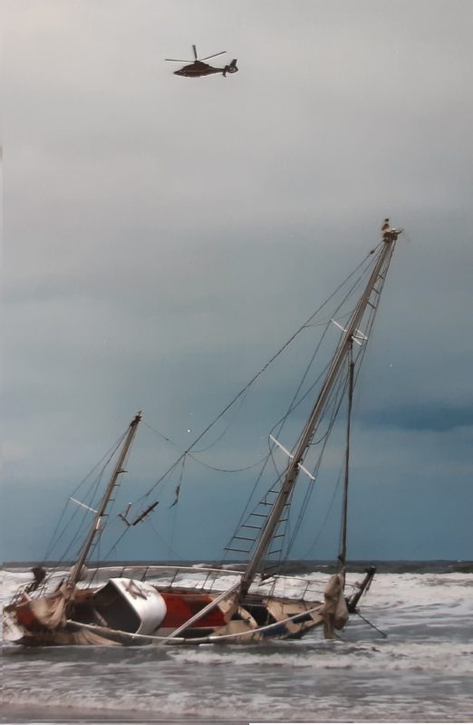 Gekenterte Segelyacht im Wasser, am Himmel ein Hubschrauber
