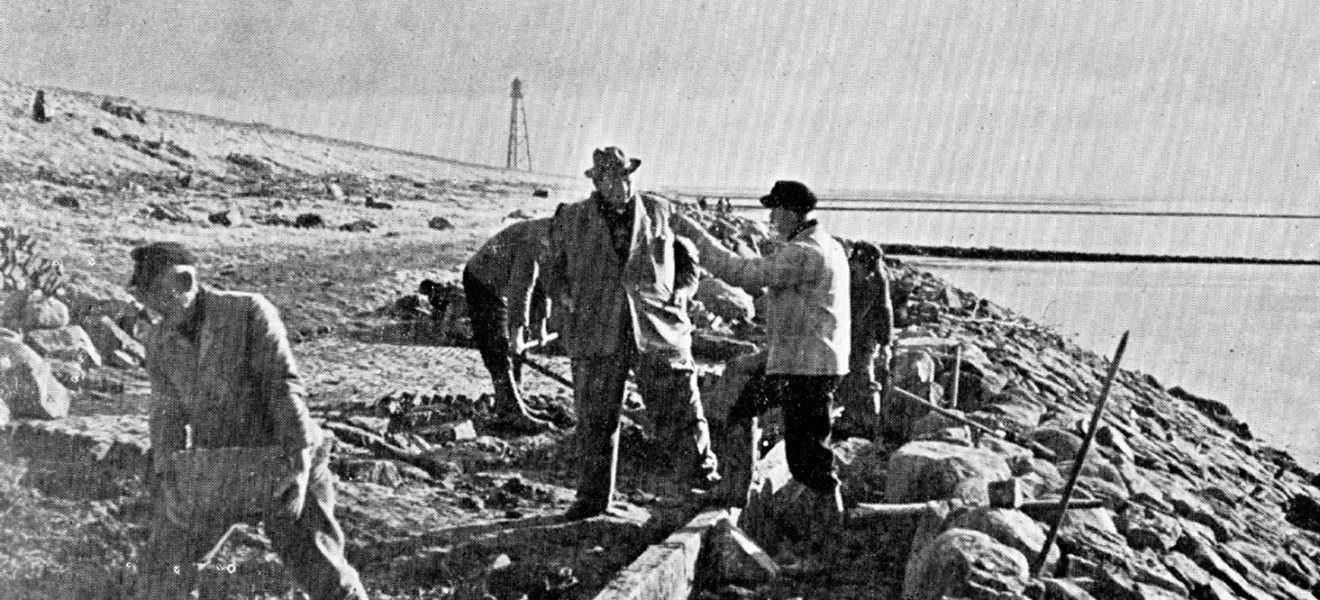 Schwarz-weiß Fotografie mit Arbeitern an einem Deich