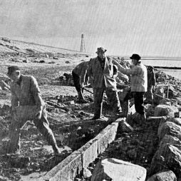 Deichbauarbeiten zwischen Upleward und Campen, mit Blick in Richtung des Campener Leuchtturms, o. J. (Archiv des Entwässerungsverbands der Deichacht Krummhörn) Schwarz-weiß Fotografie mit Arbeitern an einem Deich