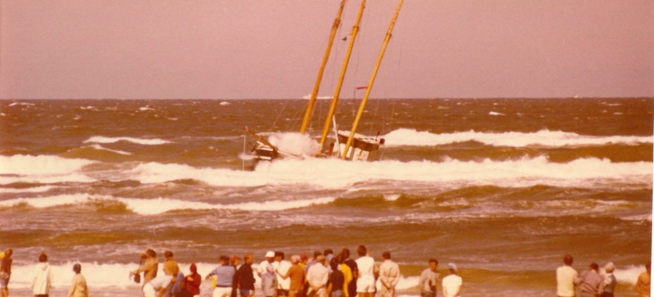 Manövrierunfähiger Dreimaster im Wasser, am Strand eine Gruppe Schaulustiger